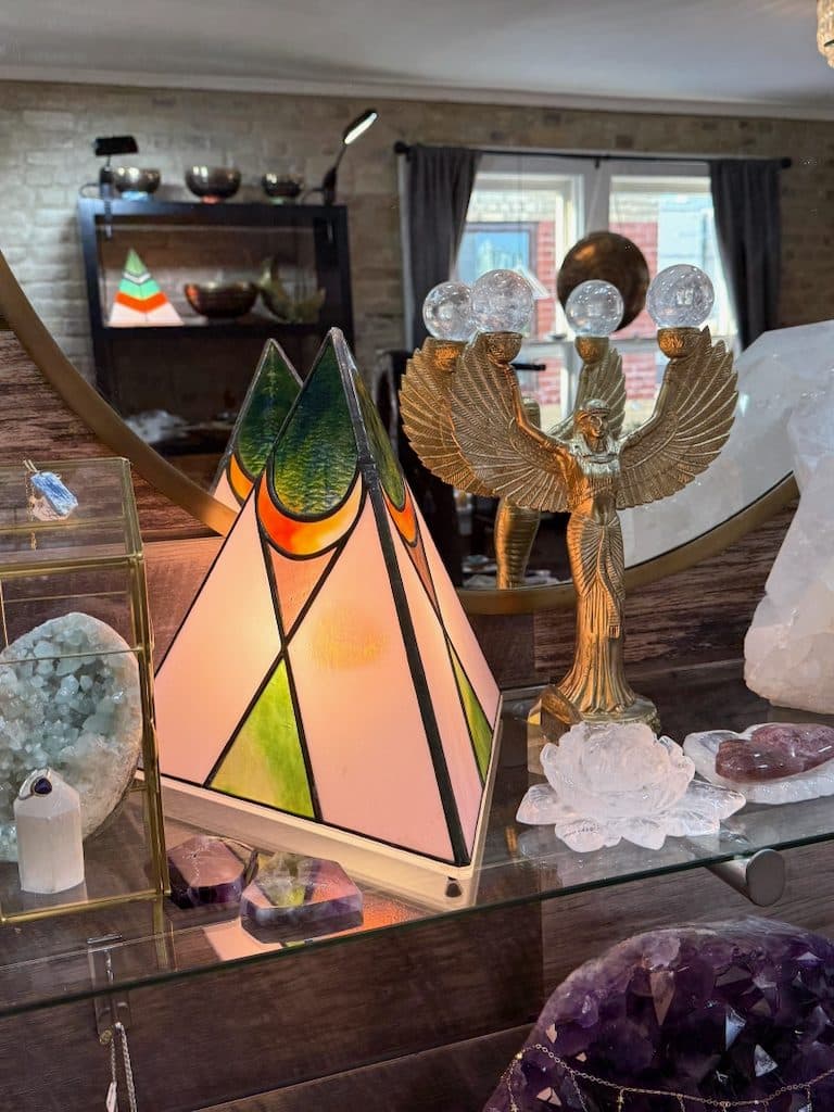 Stained glass pyramid lamp, brass winged figurine, clear quartz cluster and amethyst geode on a glass shop display