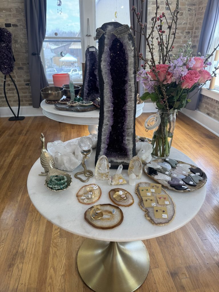 Tall amethyst geode tower on a marble table with fresh flowers and jewelry displays