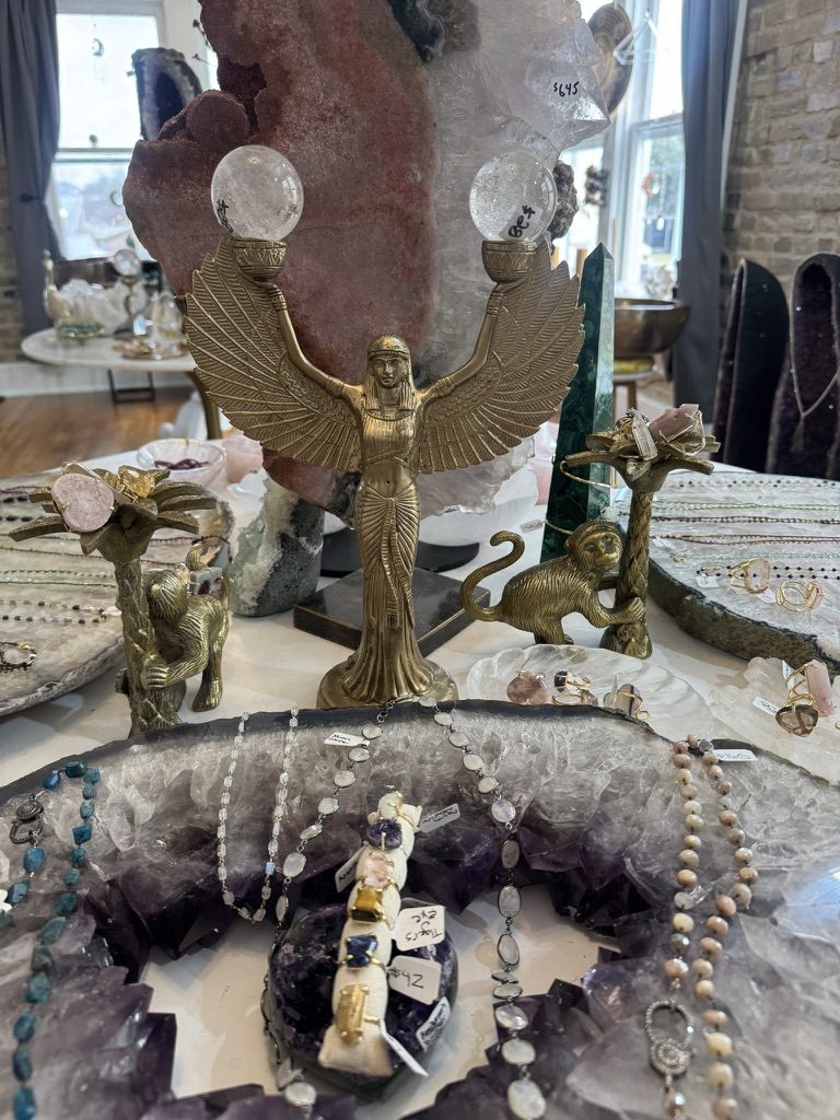 Brass winged-Isis figurine surrounded by crystal jewelry on a geode-edged display